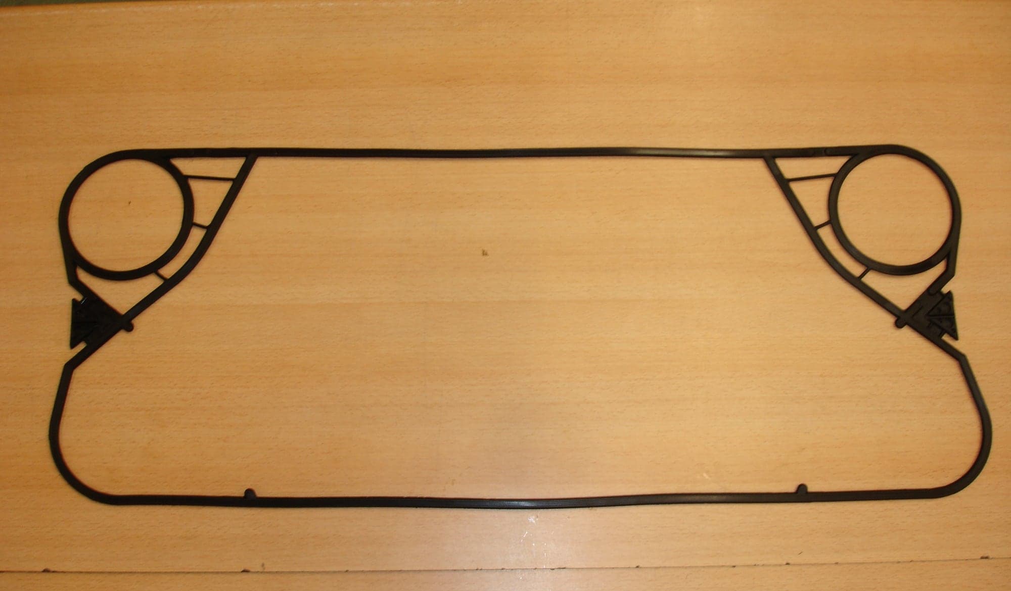 A moulded replacement gasket for a plate heat exchanger laid flat on a bench, the perimeter looping around one pair of ports to seal them out of the channel