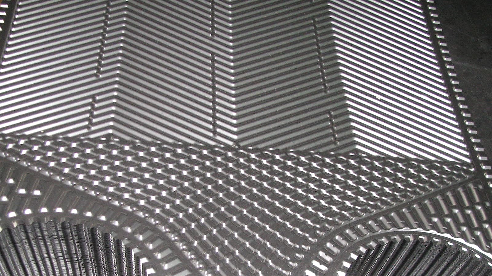 Pressed stainless plates stacked face to face, the chevron field running down into the port shoulders