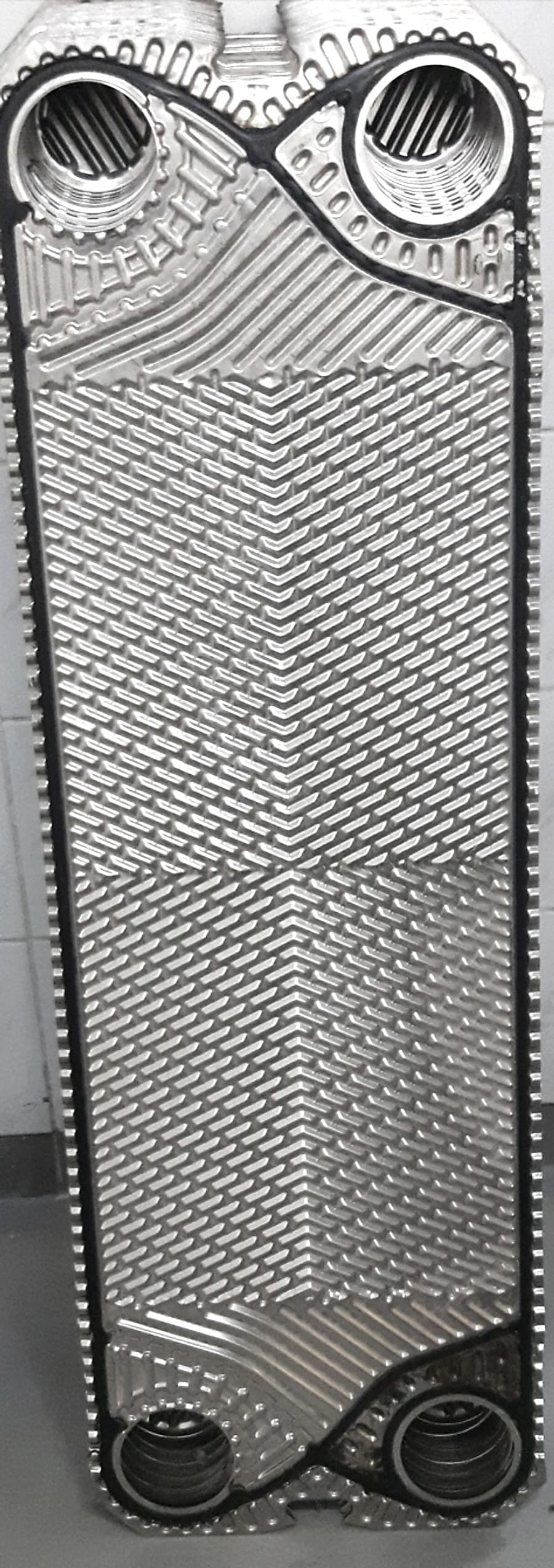 A plate with its gasket fitted. The gasket rings the top-left and bottom-right ports out of this channel and sweeps around the other two, so the fluid enters at one corner and leaves at the diagonally opposite one, which makes it a diagonal-flow plate. The next plate in the pack carries the mirror of this gasket, which is what puts the other fluid in the channel behind it.