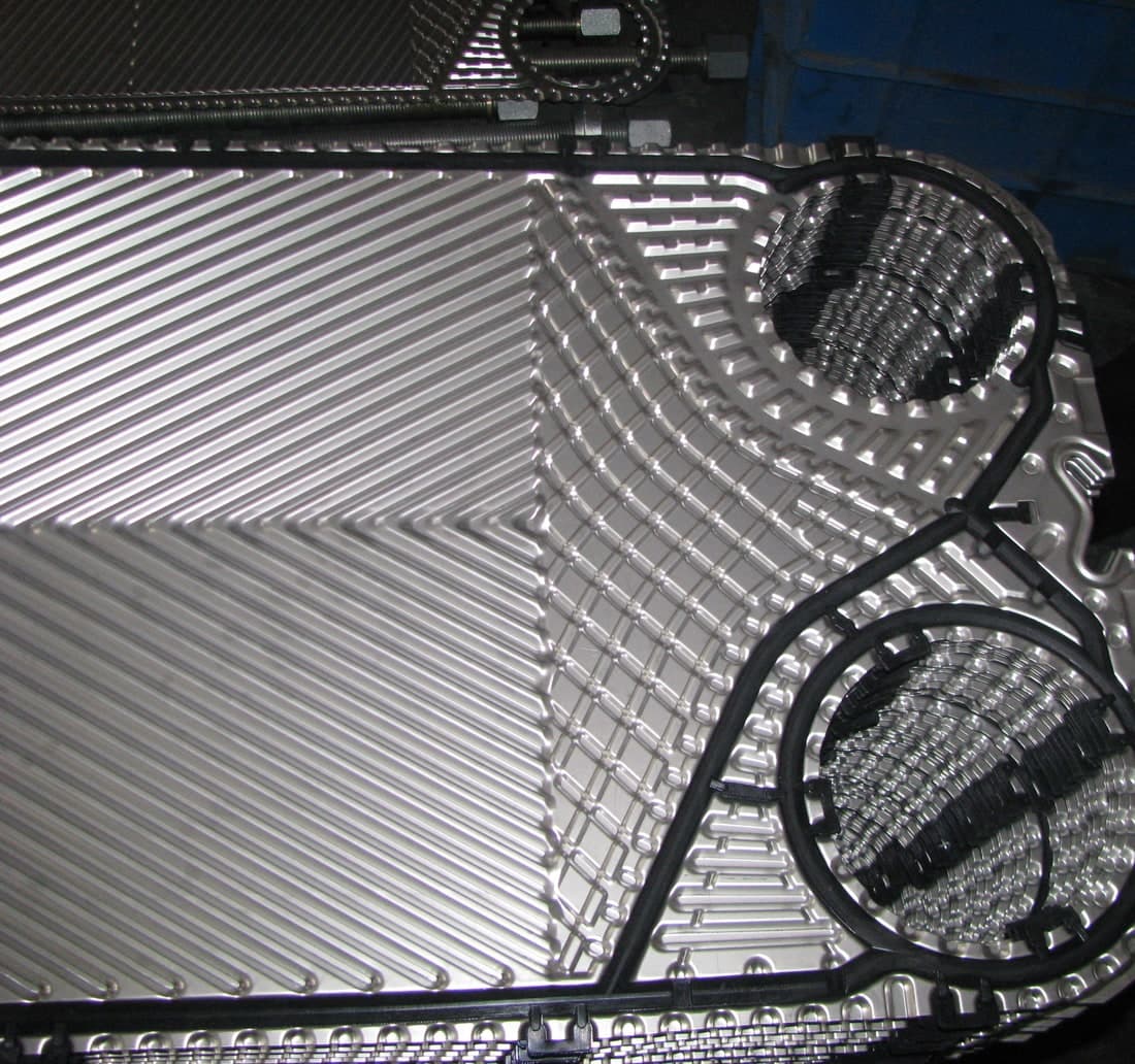 A plate with its gasket fitted, close. The gasket runs the perimeter and loops around the ports it seals out of this channel, and the chevron field it sits against is what holds the channel open.